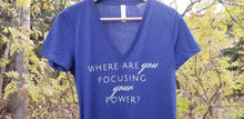 Load image into Gallery viewer, Navy vee neck tee shirt hanging from a branch in the forest with the words Where are you focusing your power in white font
