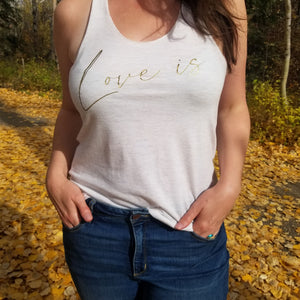 A model in a forest is wearing a oatmeal coloured  tank top with the words Love is in gold font 