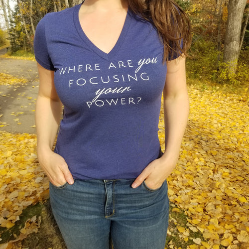 A model in a forest is wearing a navy v-neck tee shirt with the words  Where are you focusing your power 