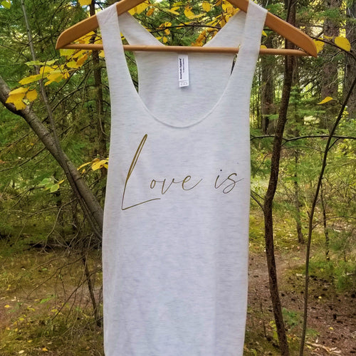 An oatmeal coloured tank top hanging from a branch with  the words Love is in gold letters